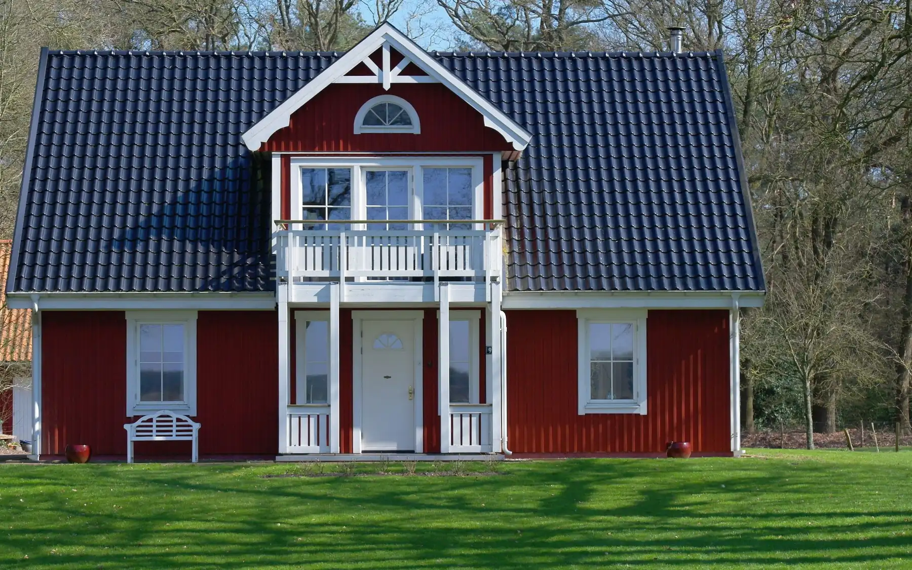 Rødt hus med hvit balkong og pyntet gavl foran en grønn plen